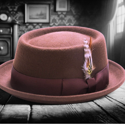 A brown pork pie hat with a purple feather decoration rests on a wooden floor in a dimly lit room with vintage furniture and framed pictures on the wall. The background appears in grayscale, contrasting with the hat's color.