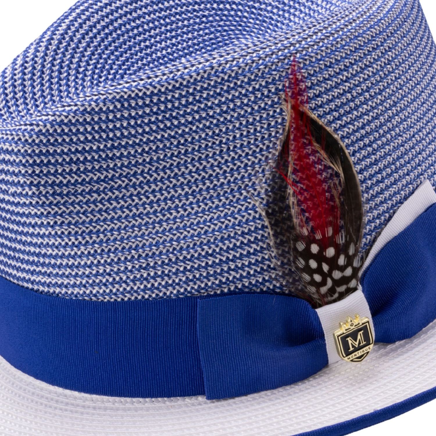 Close-up of the dual-tone grosgrain ribbon, signature Montique metal pin, and feather accent on a royal fedora.