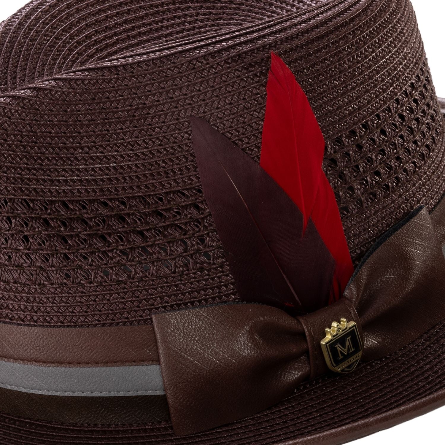 Close-up of brown mesh fedora showing the striped satin ribbon, signature red feather, and Montique metal crest pin.