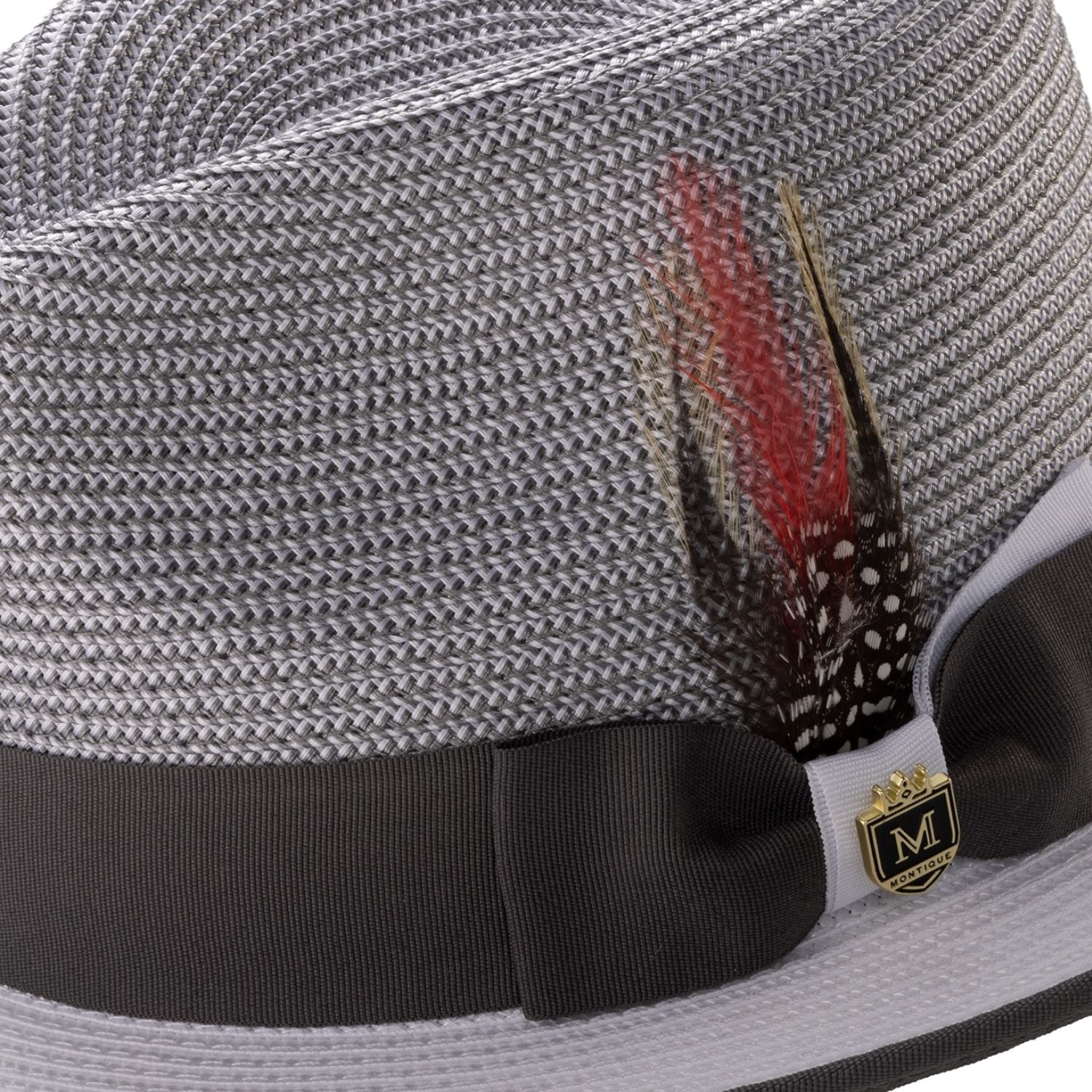 Close-up of the dual-tone grosgrain ribbon, signature Montique metal pin, and feather accent on a grey fedora.