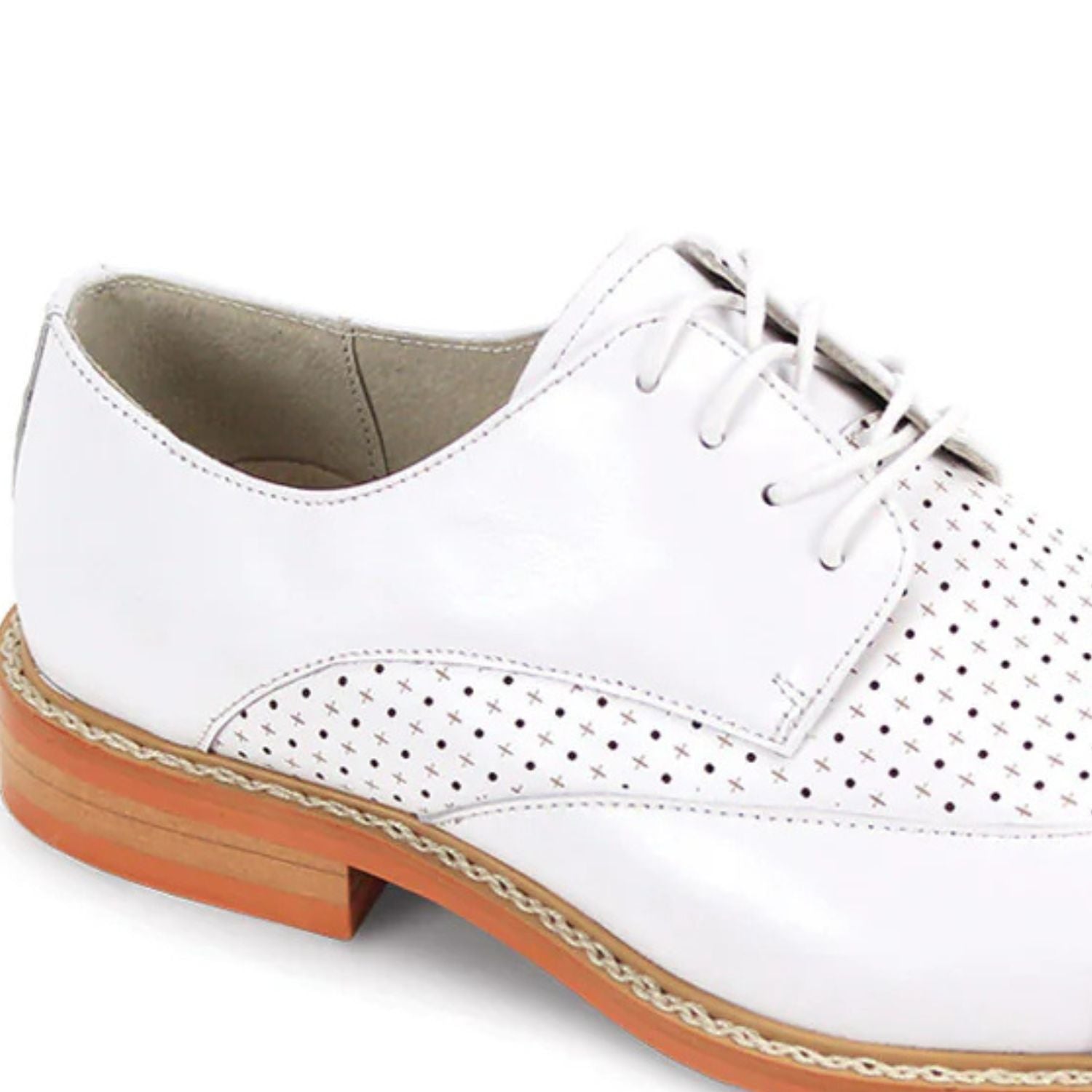Close-up of intricate laser perforated pattern and brogue detailing on white leather shoe.
