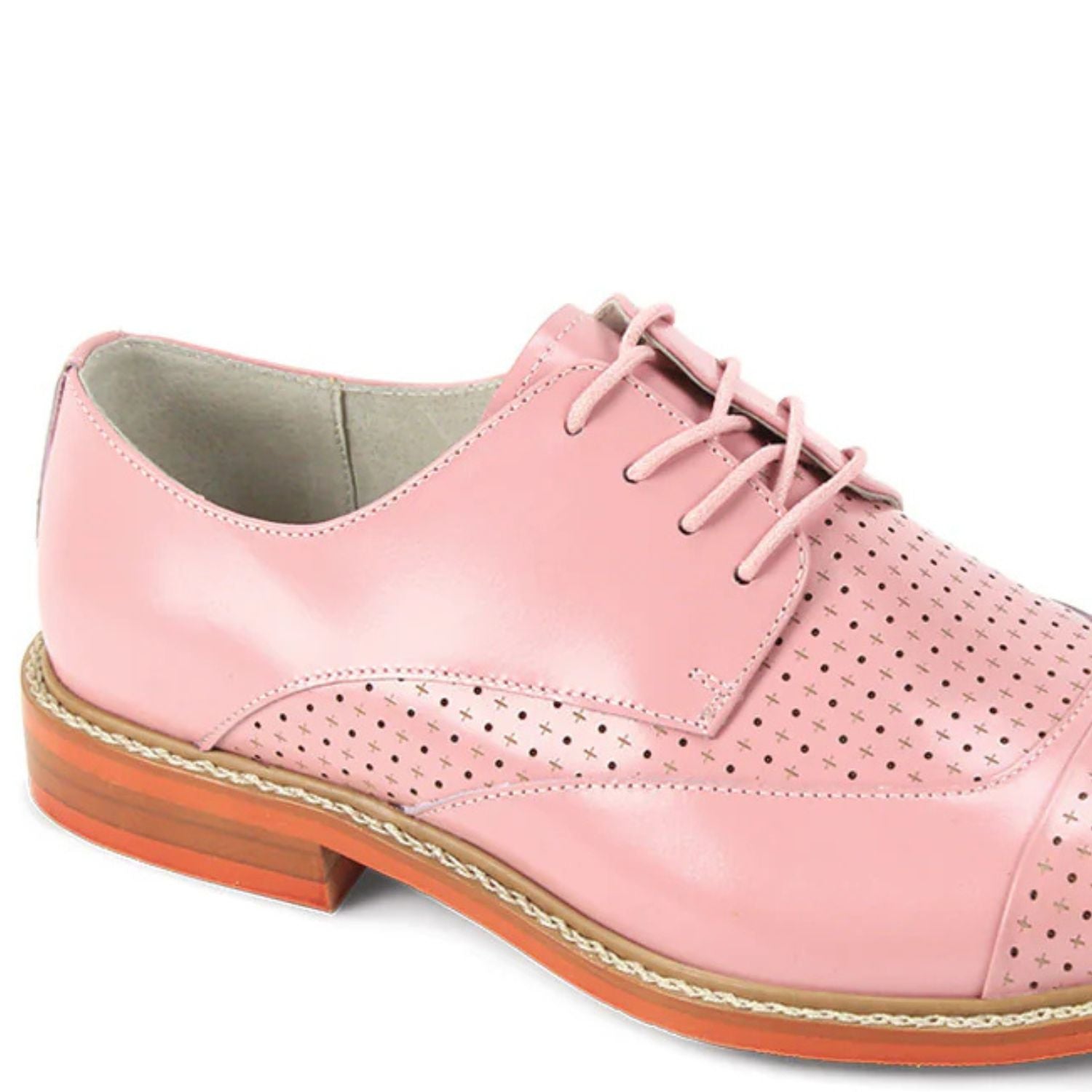 Close-up of intricate laser perforated pattern and brogue detailing on pink leather shoe.