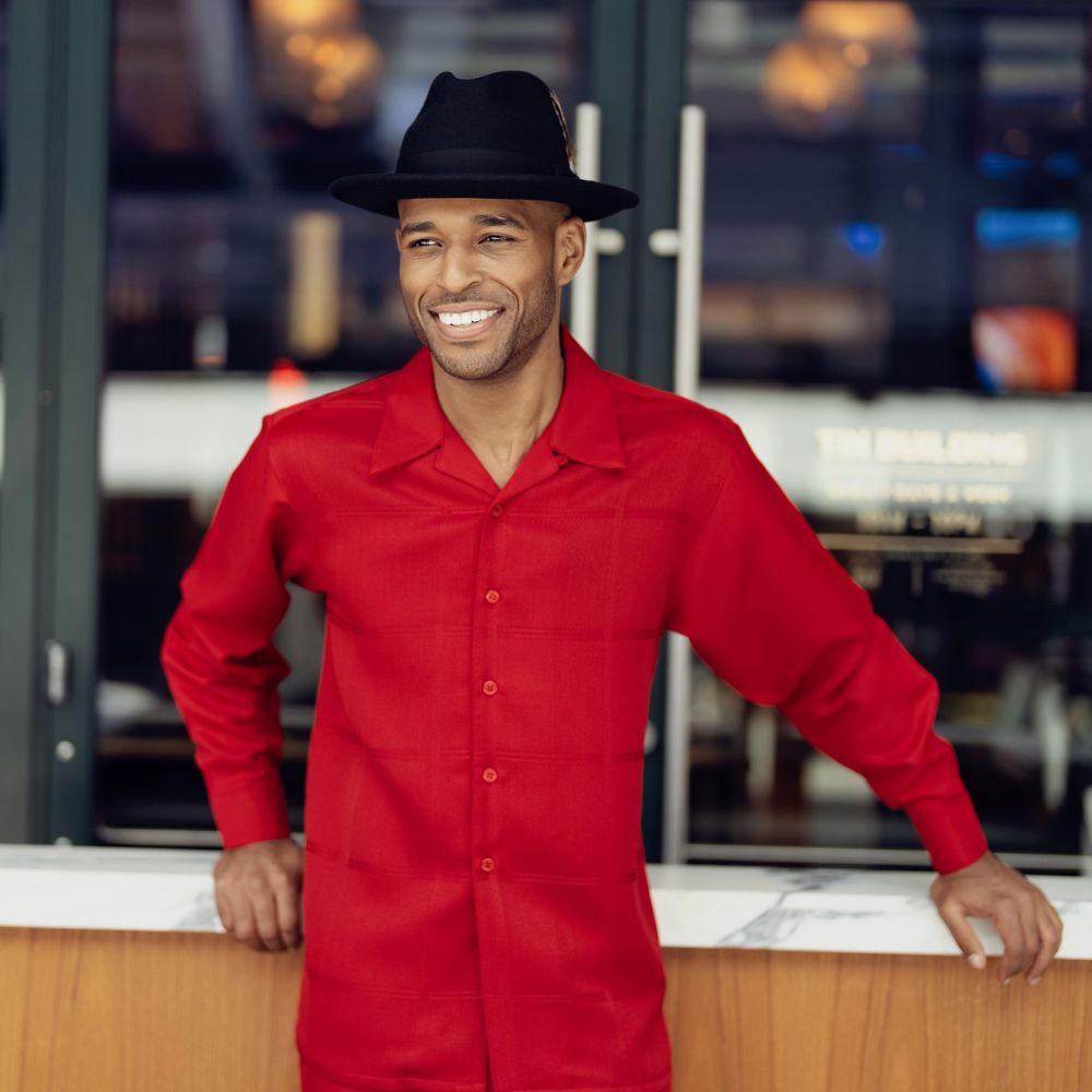 a man wearing a montique's red long-sleeve walking suit and a black fedora.