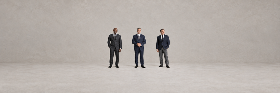 Three men in charcoal and navy suits and a navy blazer with charcoal trousers, white shirts, dark ties, and black dress shoes.
