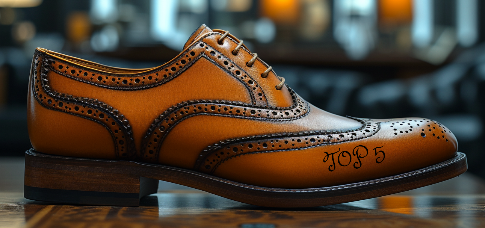 A close-up of a polished brown brogue shoe on a wooden surface. The words 'Top 5' are engraved on the heel. The background is blurred, suggesting an indoor setting with warm lighting.