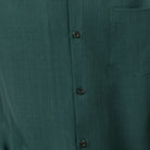 Close-up of emerald green 100% polyester fabric showing the solid texture and button detail