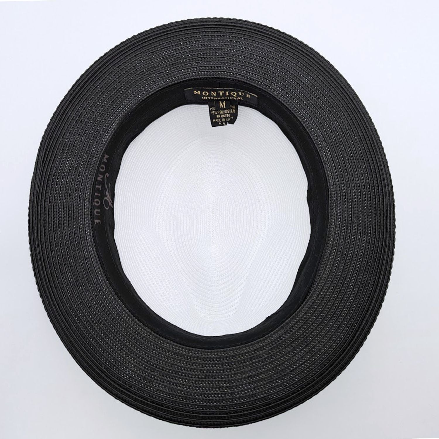 Black and white Montique fedora hat interior view with black woven brim, black sweatband, white crown, and branded label