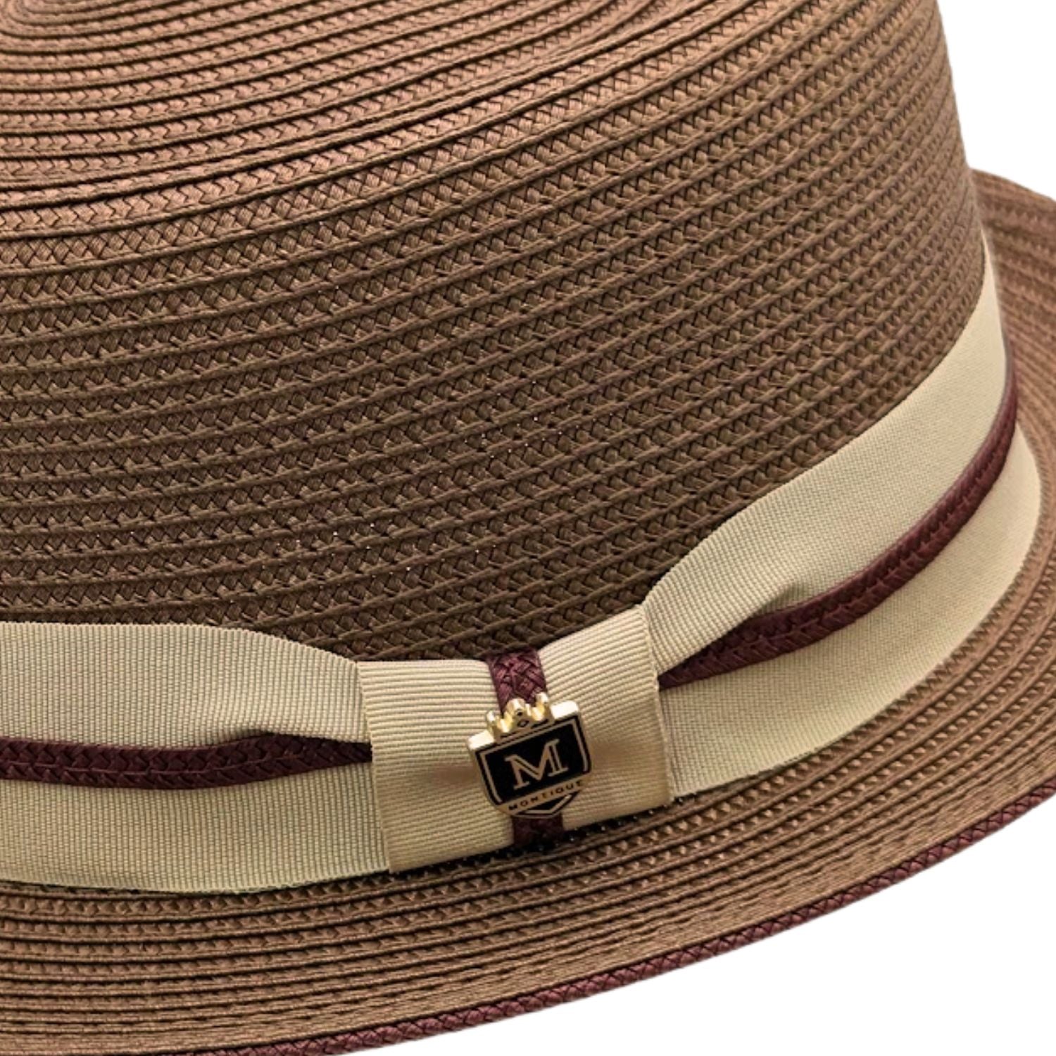 Close-up of cappuccino Montique pork pie straw hat showing woven texture, beige band, burgundy cord trim, and logo pin