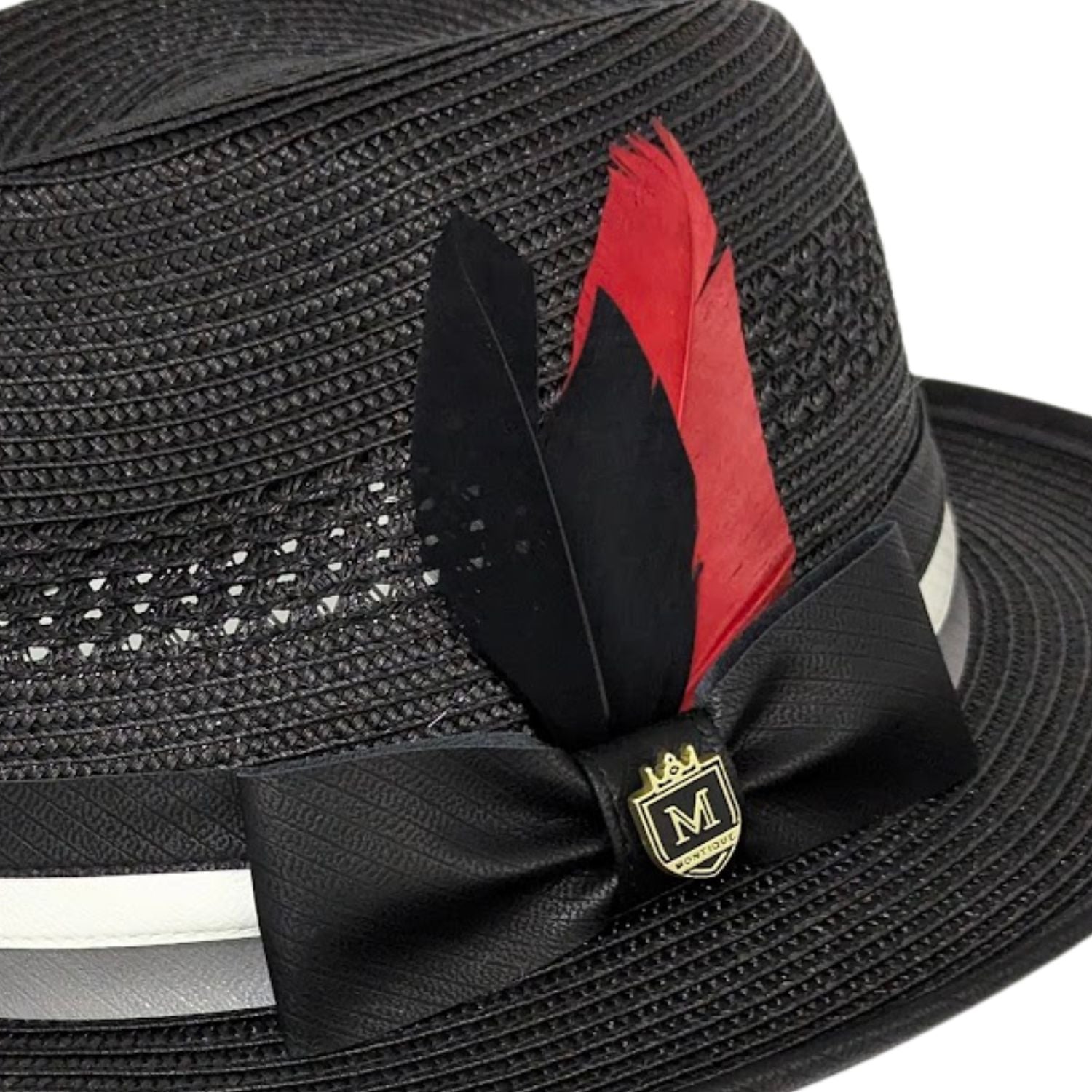 Close up of black Montique fedora hat with black bow, red and black feathers, woven texture, and gold logo pin