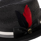 Close-up of black mesh fedora showing the striped satin ribbon, signature red feather, and Montique metal crest pin.