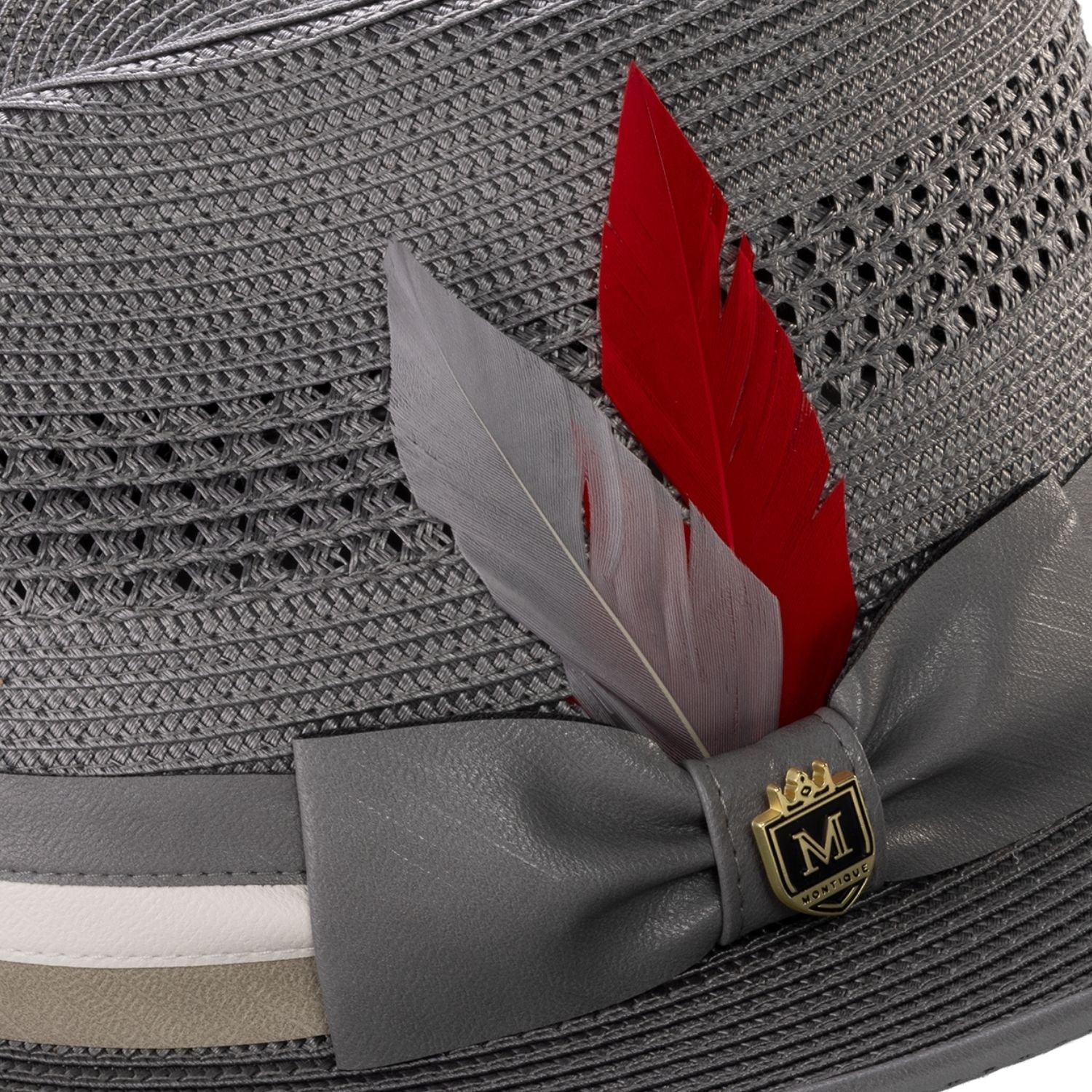 Close-up of grey mesh fedora showing the striped satin ribbon, signature red feather, and Montique metal crest pin.