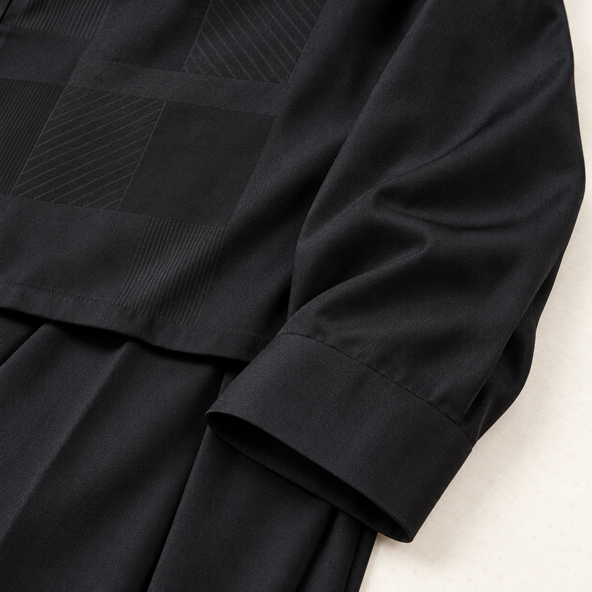Smooth black sleeve and cuff of a Montique tonal patchwork walking suit arranged over matching black trousers.